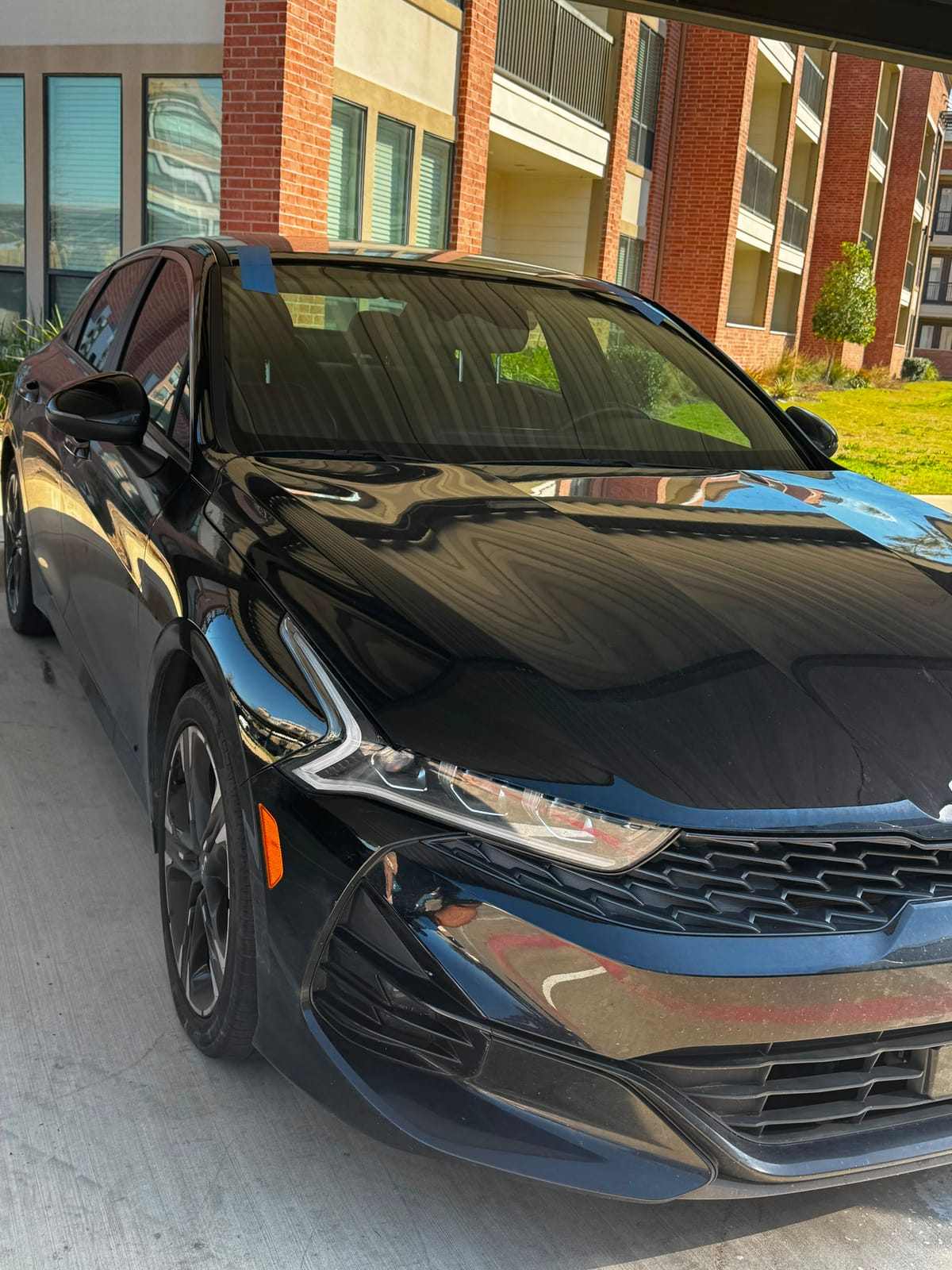 Glossy black Kia K5 sedan with freshly tinted windows parked under a carport