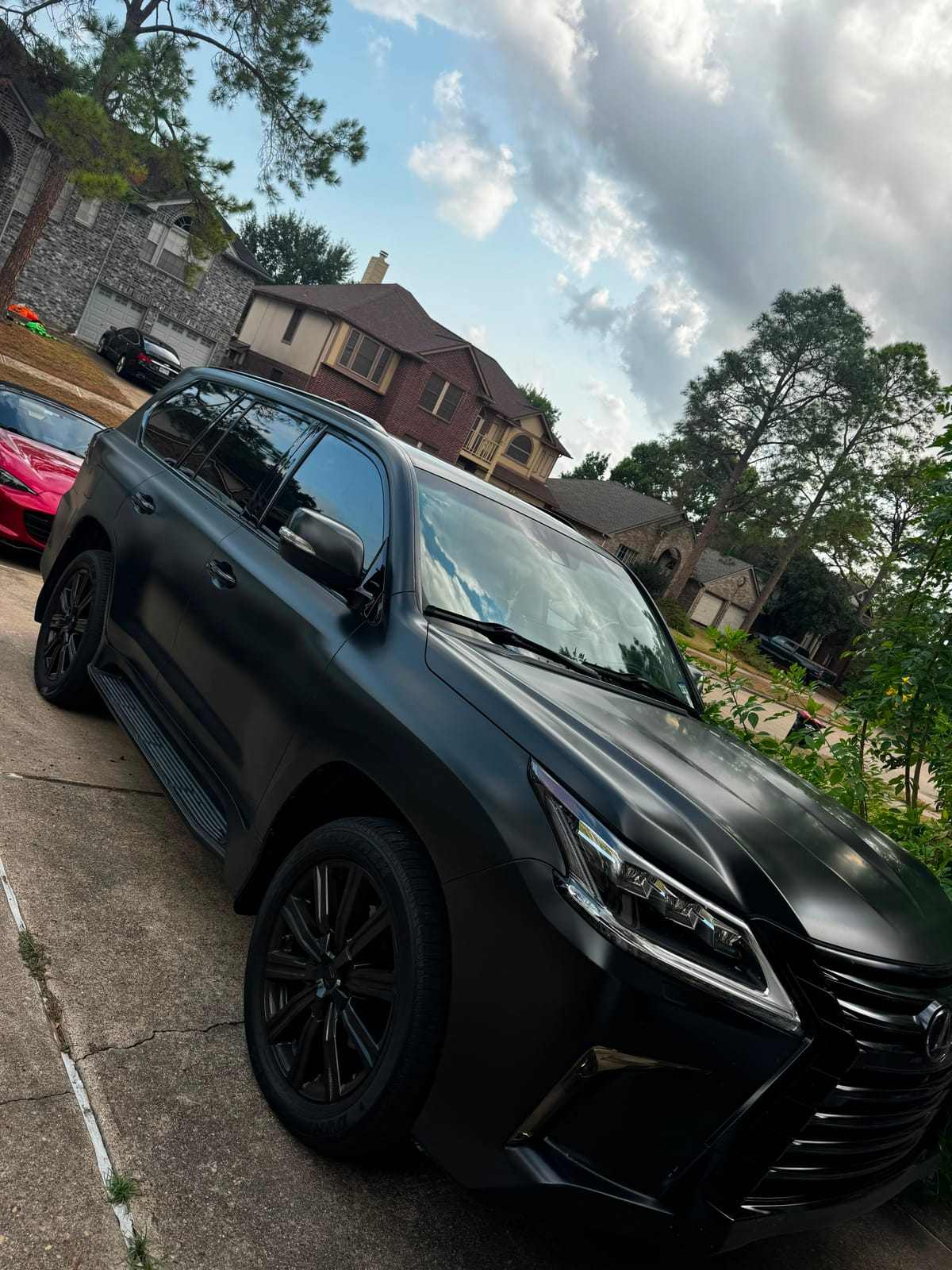 Matte black Lexus LX 570 SUV with dark window tint parked in a residential driveway