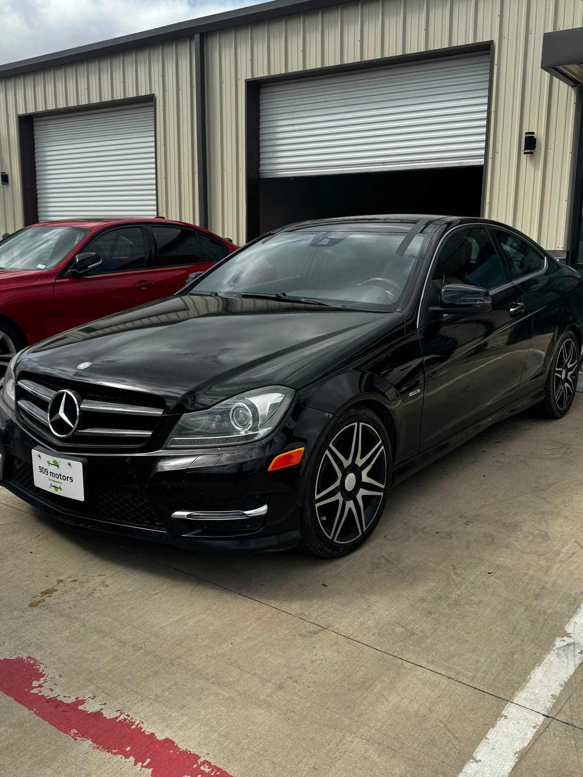 Black Mercedes-Benz C-Class coupe with tinted windows parked outside the shop